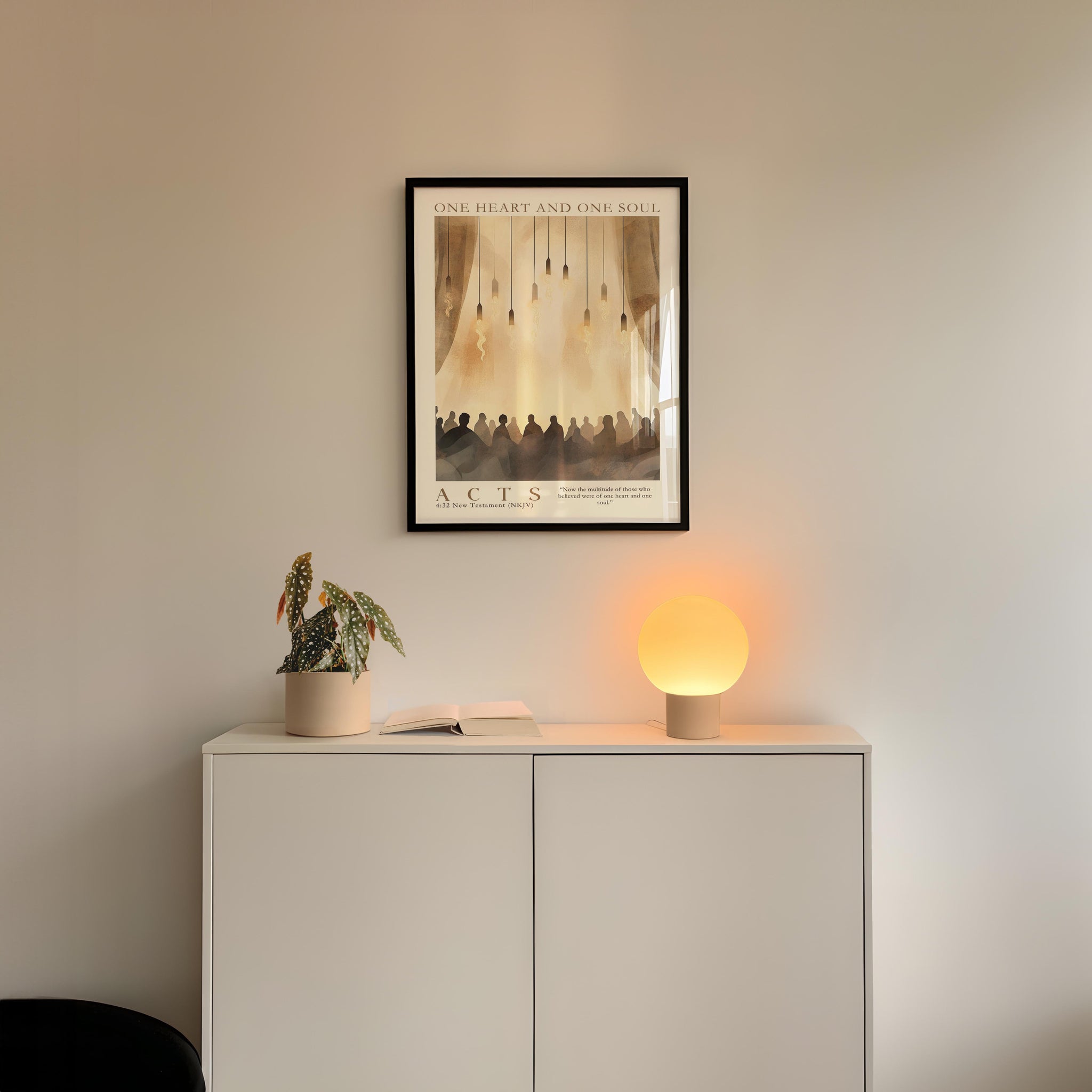a minimalist interior design with a framed poster of a group of people hanging on a white wall above a white cabinet. The cabinet has a plant and a lamp on it, creating a cozy and inviting atmosphere.