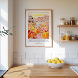 a kitchen scene with a framed poster of a colorful garden hanging on the wall above a wooden countertop with a bowl of lemons.