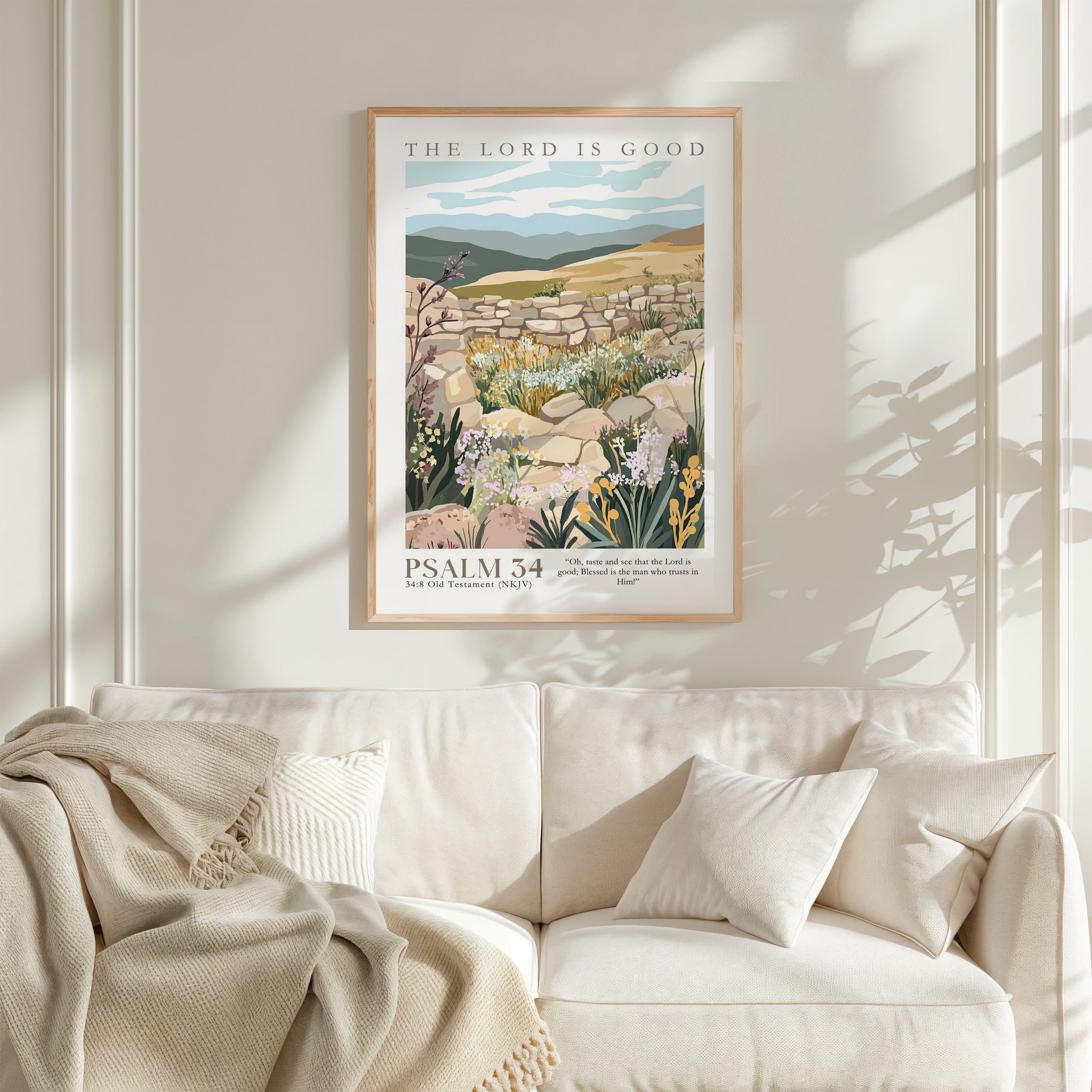 a framed poster of a pastoral landscape with a mountain backdrop, hanging on a wall above a white couch with a blanket draped over it.