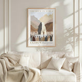 a framed poster of a mountain landscape with a group of people gathered around it, hanging on a wall above a white couch.
