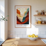 a kitchen counter with a bowl of lemons, a framed poster of a mountain landscape, and a shelf with jars and other kitchen items.