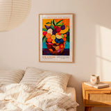 a framed poster of a colorful fruit arrangement hanging on a wall above a bed with striped pillows.