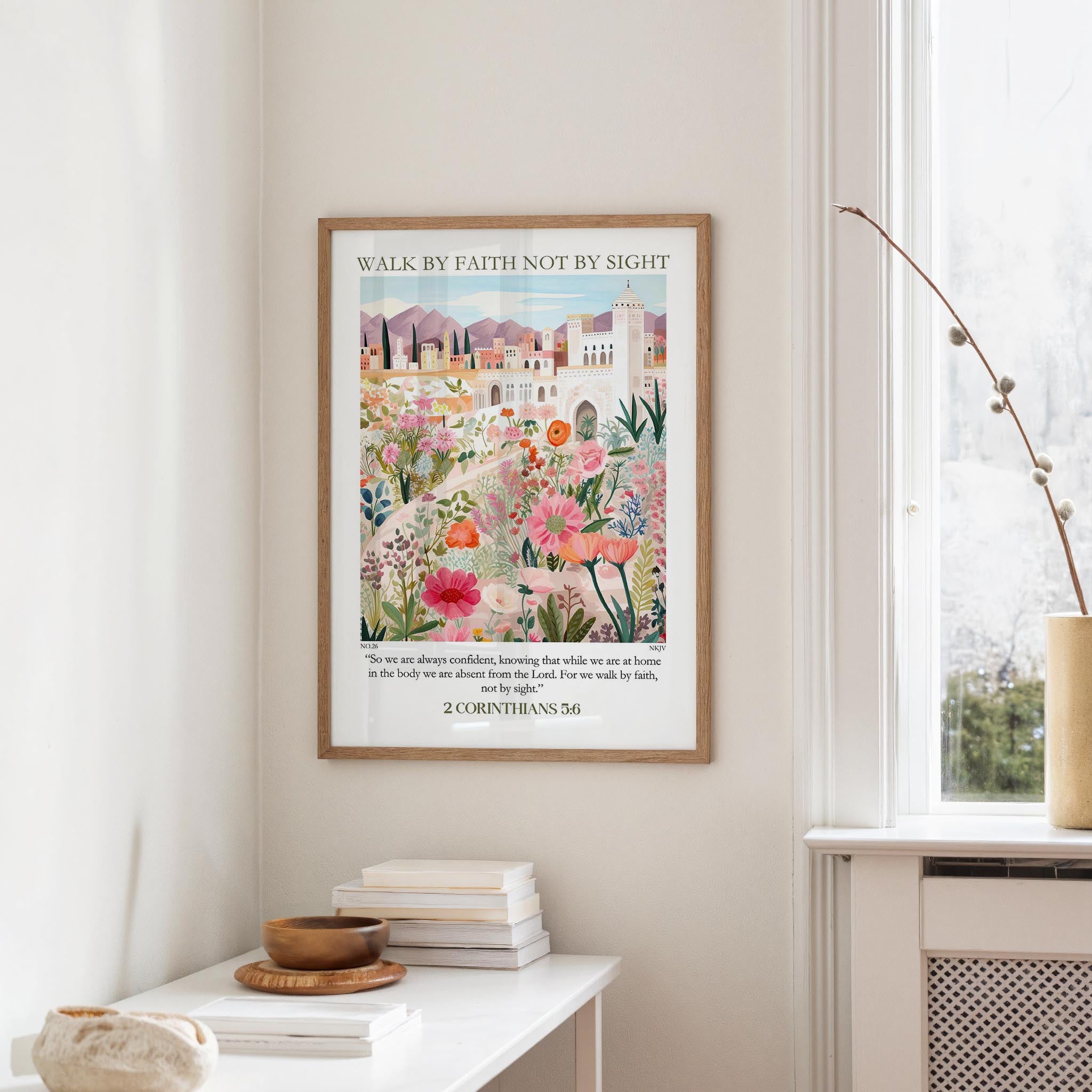 a framed poster of a colorful floral scene hanging on a wall, with a window and a small table with books and a bowl in the foreground.