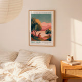 a bedroom scene with a framed poster of a landscape hanging on the wall above a bed with striped pillows.