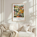 a framed poster of a vibrant floral scene hanging on a wall above a white couch with a blanket draped over it.
