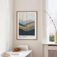 a framed poster of a mountain landscape hanging on a wall, with a stack of books and a vase on a table below it.