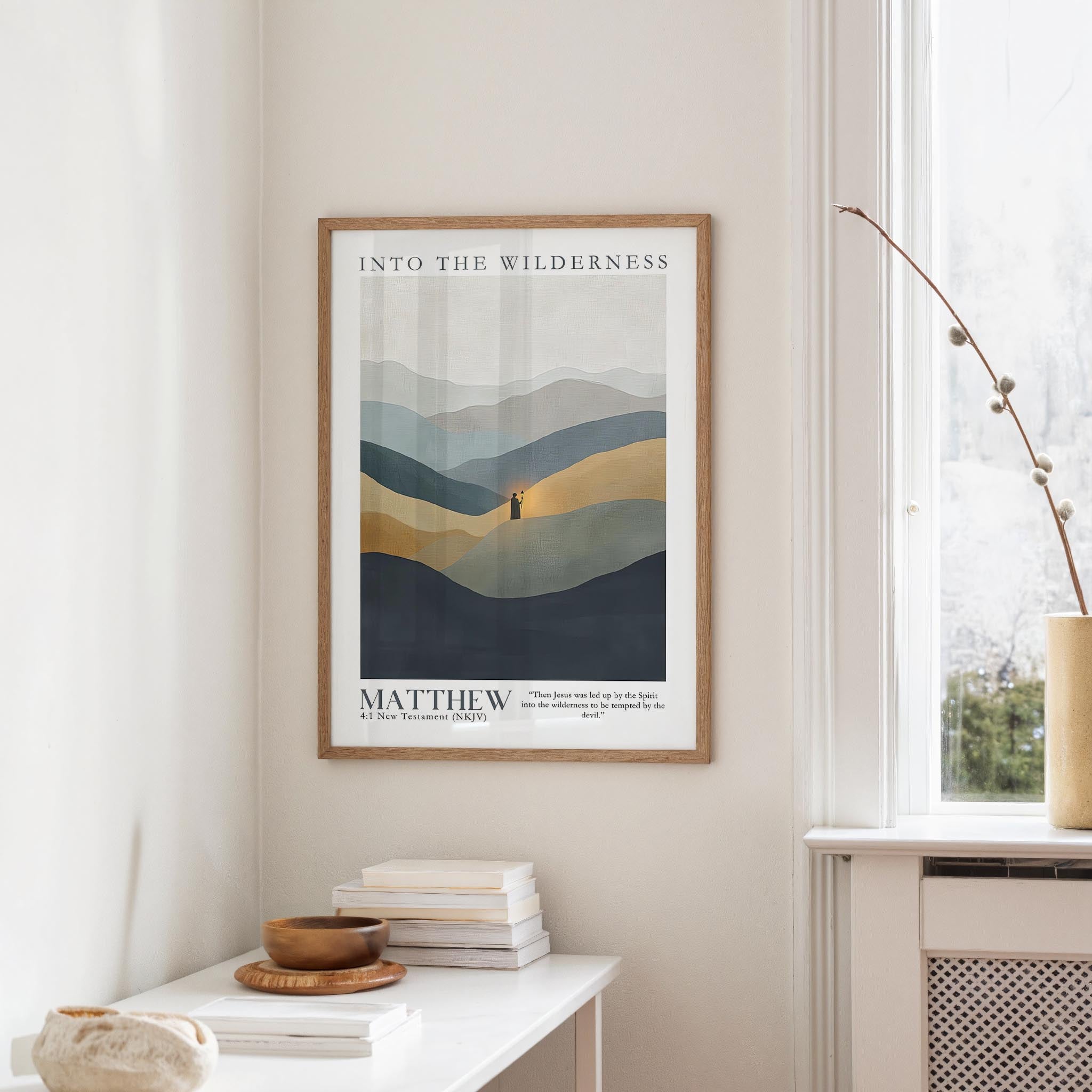 a framed poster of a mountain landscape hanging on a wall, with a stack of books and a vase on a table below it.
