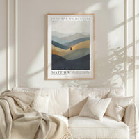 a framed poster of a landscape with mountains and a person standing in the middle, hanging on a wall above a white couch with a blanket draped over it.