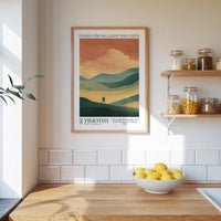 a kitchen counter with a bowl of lemons, a framed poster of a mountain landscape, and a shelf with jars and bottles.