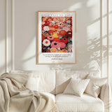 a framed poster of a vibrant floral arrangement hanging on a white wall above a white couch with a blanket draped over it.