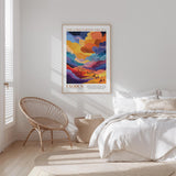 a bedroom with a bed, a woven chair, and a poster of a colorful landscape hanging on the wall.