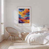 a bedroom with a bed, a woven chair, and a poster of a colorful landscape hanging on the wall.