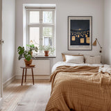 a cozy bedroom with a large bed, a nightstand with a plant, and a framed poster on the wall.