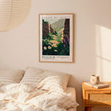 a bedroom scene with a framed poster of a mountain landscape hanging on the wall above a bed with striped pillows.