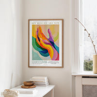 a colorful abstract painting hanging on a wall, with a stack of books and a vase on a table below it.