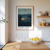 a framed poster of a whale with a person inside, hanging on a wall above a wooden counter with a bowl of lemons.