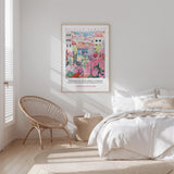 a bedroom with a large poster of a colorful cityscape hanging on the wall above a bed with white bedding. The room has a wicker chair and a small side table, creating a cozy and inviting atmosphere.