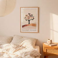 a bedroom scene with a framed poster of a tree on the wall above a bed with striped bedding. There is also a wooden nightstand with a coffee mug and a book on it.