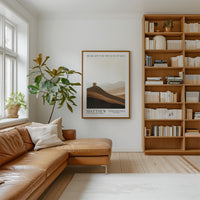 a cozy living room with a large bookshelf filled with books, a comfortable leather sofa, and a framed poster of a mountain landscape.