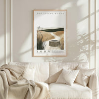 a framed poster of a serene landscape with a well in the center, hanging on a wall above a white couch with a blanket draped over it.
