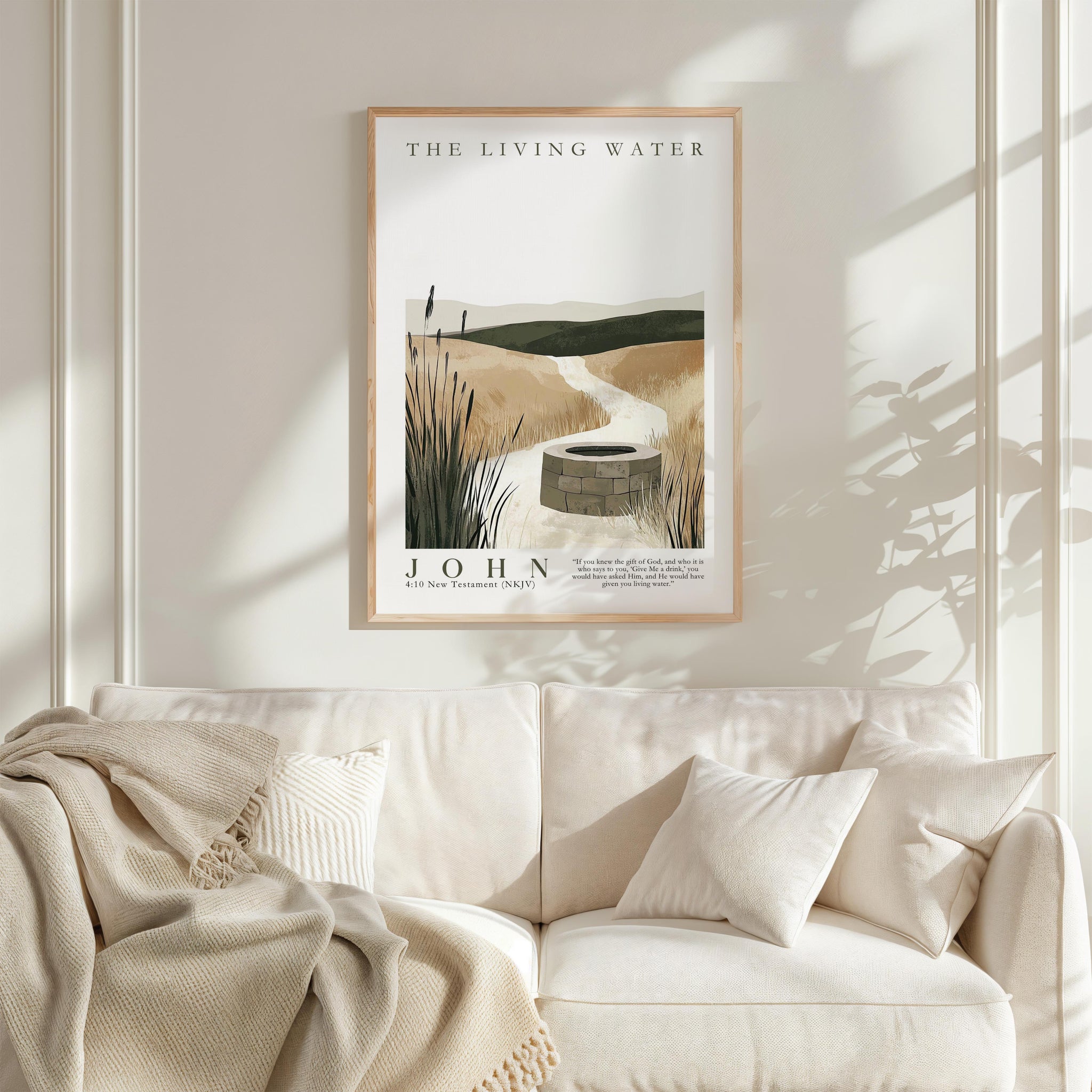 a framed poster of a serene landscape with a well in the center, hanging on a wall above a white couch with a blanket draped over it.