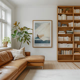 a cozy living room with a brown leather sofa, a large window, a wooden bookshelf filled with books, and a framed poster on the wall.