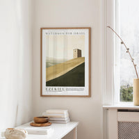 a framed poster of a desert landscape with a small tower in the background, hanging on a wall above a white table with a stack of books and a small vase.