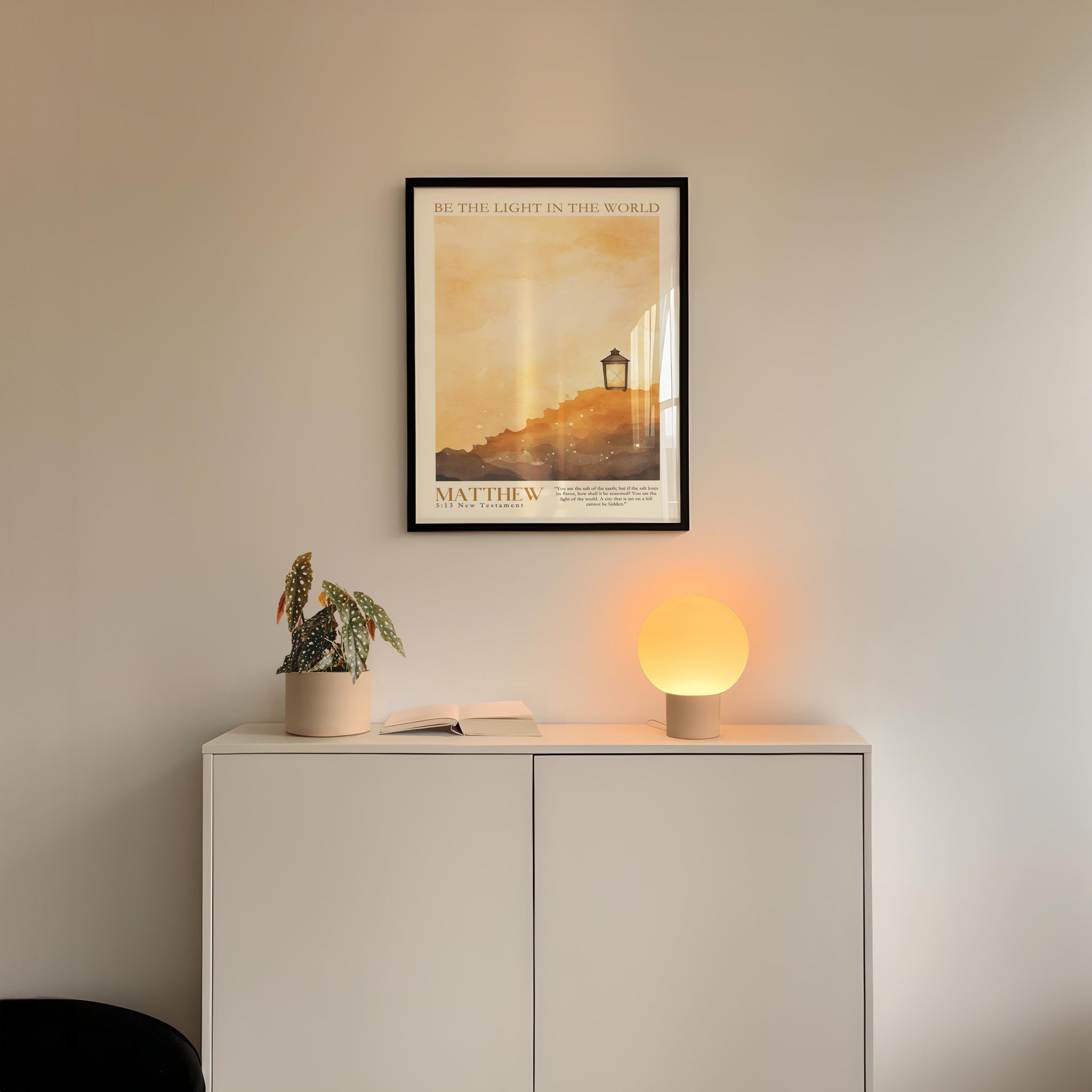 a minimalist interior design with a framed poster of a lighthouse, a potted plant, and a small lamp on a white cabinet.