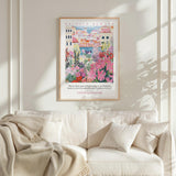 a framed poster of a colorful garden scene hanging on a wall above a white couch with a blanket draped over it.