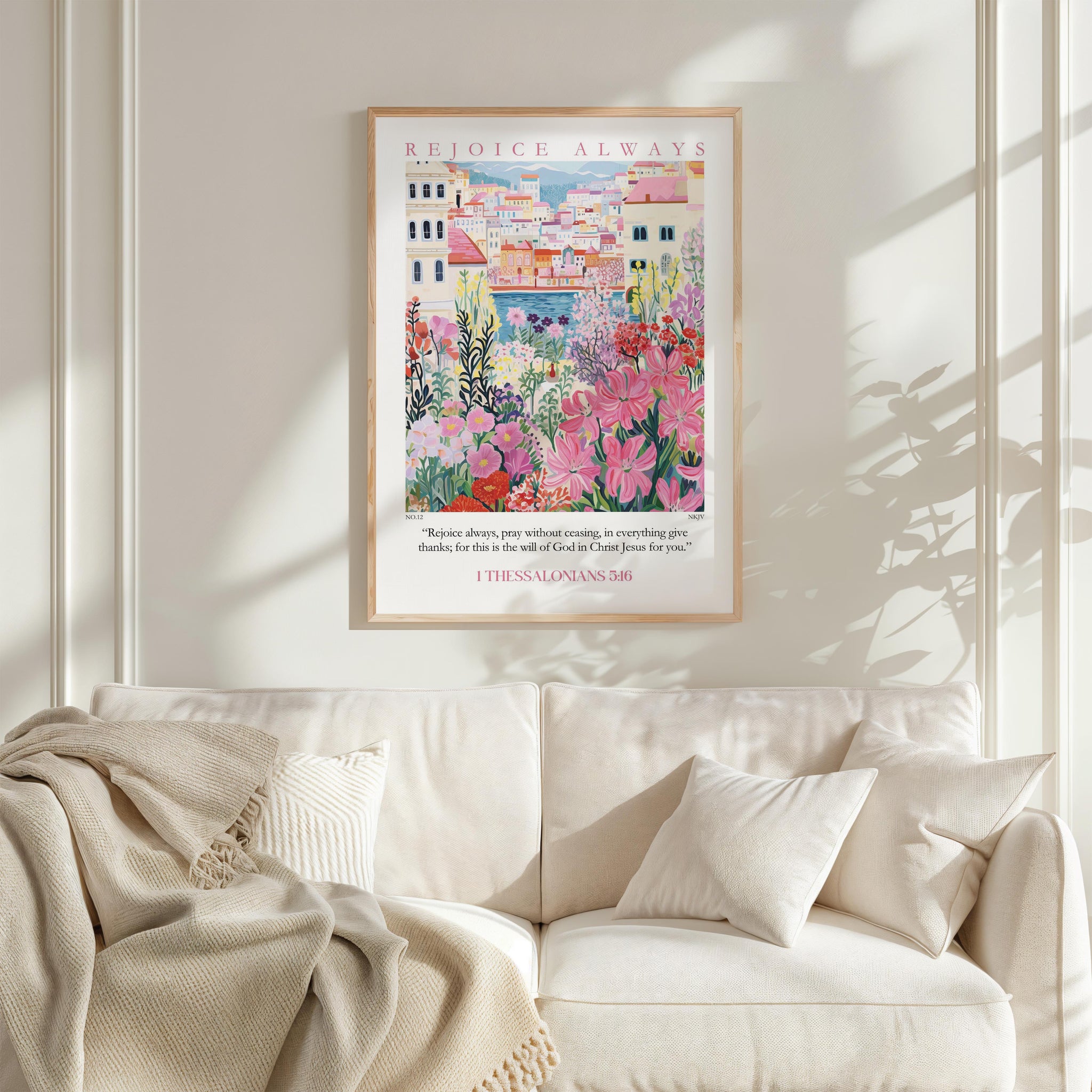 a framed poster of a colorful garden scene hanging on a wall above a white couch with a blanket draped over it.