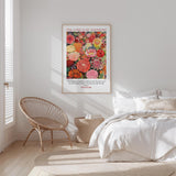 a bedroom with a bed, a woven chair, and a framed poster of a colorful floral design on the wall.