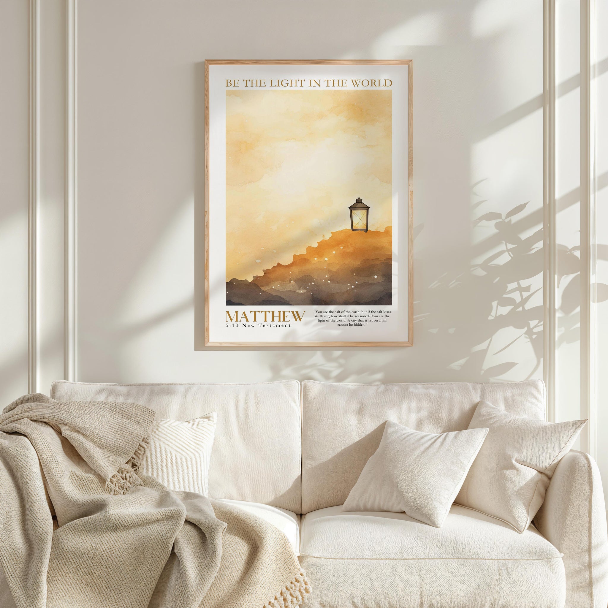 a framed poster of a serene landscape with a lantern on a hill, hanging on a white wall above a white couch with a blanket draped over it.