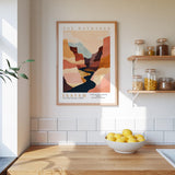 a kitchen counter with a bowl of lemons, a framed poster of a mountain landscape, and a shelf with jars and other kitchen items.
