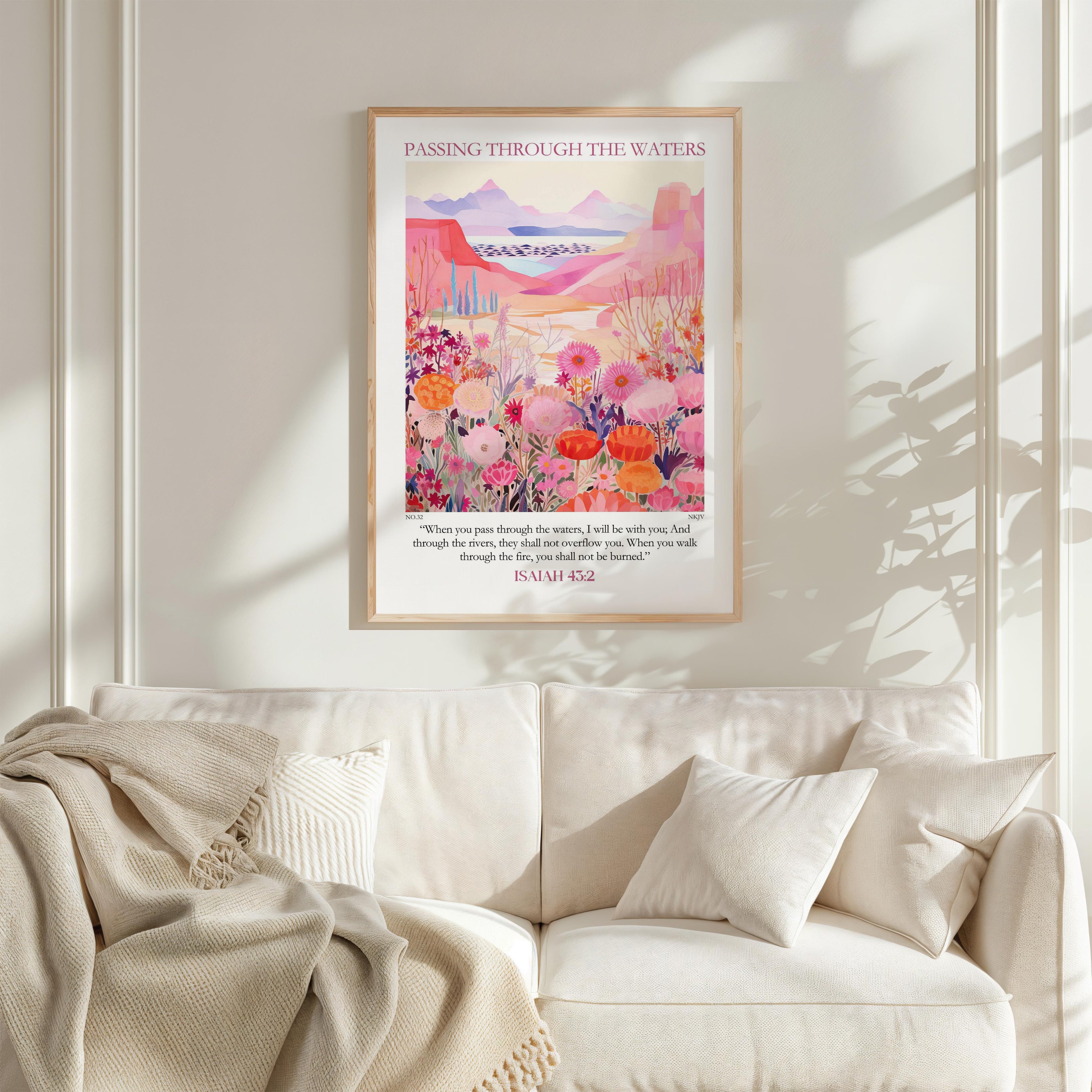 a framed poster of a vibrant, colorful landscape with flowers and mountains, hanging on a wall above a white couch with a blanket draped over it.