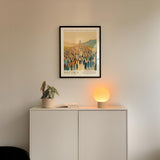 a white cabinet with a plant and a lamp on top, and a framed poster of a group of people hanging on the wall above the cabinet.