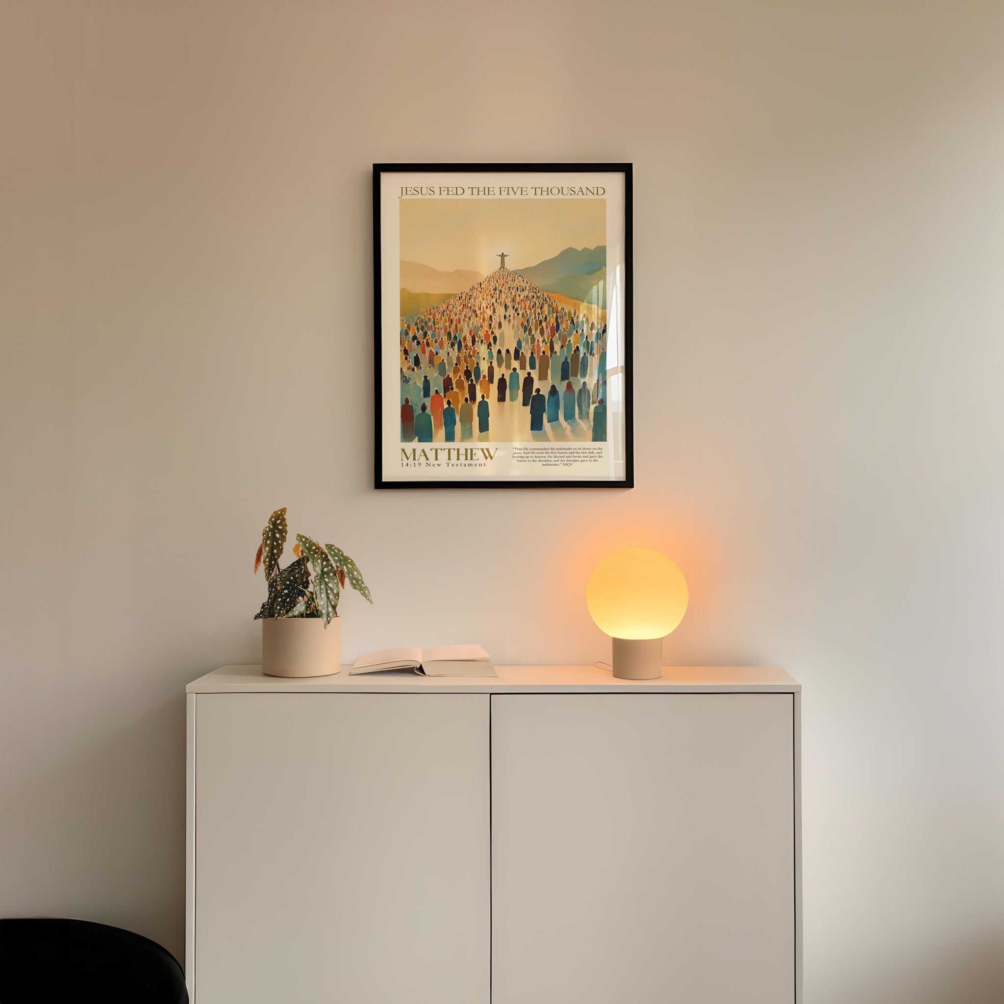 a white cabinet with a plant and a lamp on top, and a framed poster of a group of people hanging on the wall above the cabinet.