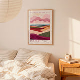 a bedroom setting with a framed poster of a landscape hanging on the wall above a bed with striped pillows.
