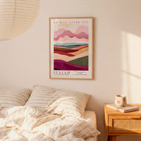 a bedroom setting with a framed poster of a landscape hanging on the wall above a bed with striped pillows.